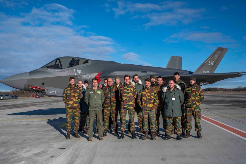 Troops stand in front of a jet.