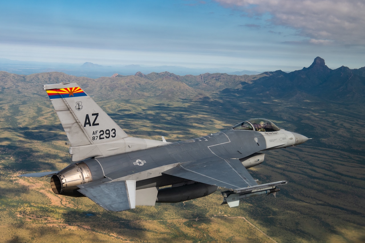 A fighter jet flies above mountainous terrain.