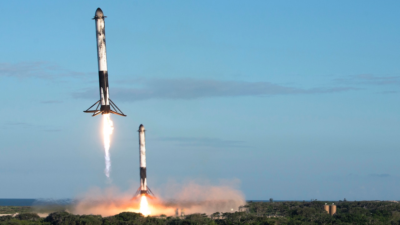 Two reusable rocket boosters land during daylight.