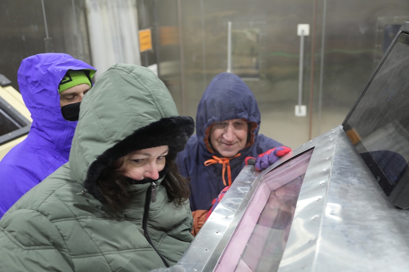 People wearing jackets and gloves observe a machine in a cold room.