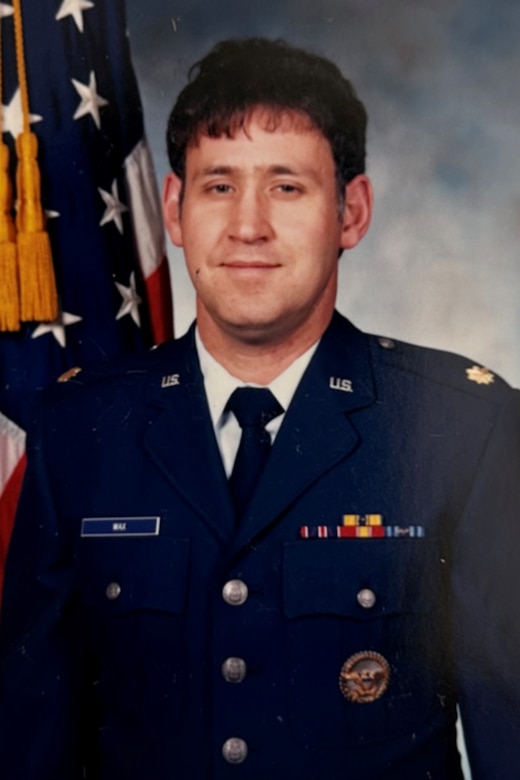 A person in an Air Force uniform poses for photo in front of a U.S. flag.
