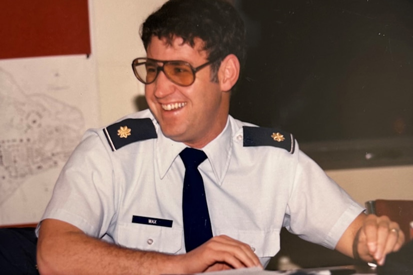 A person in an Air Force uniform sitting at a table laughs.