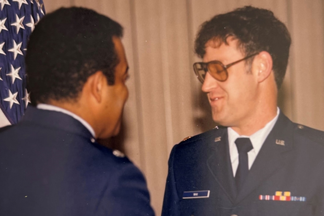 Two people in Air Force uniforms shake hands. The airman on the right wears a pinned medal.