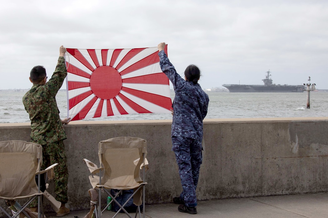 JMSDF Sailors hold a Japanese flag as USS George Washington (CVN 73) departs Naval Station Norfolk.