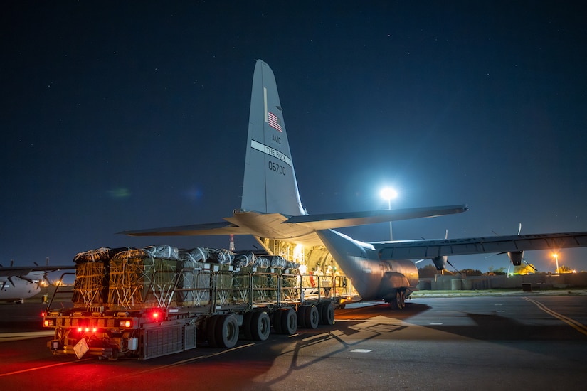 Pallets of humanitarian assistance are staged near the ramp of a military aircraft.