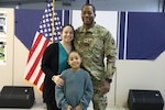 Uniformed service member smiles and stands with wife and daughter at promotion ceremony.