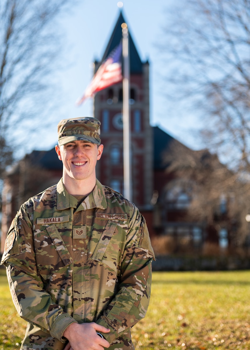 Airman stands in front of flag pole and clock tower at University of New Hampshire.
