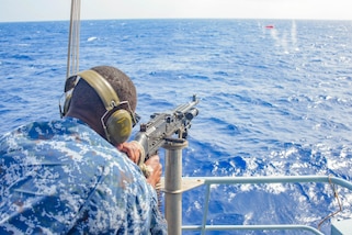 A Barbados Coast Guard member shoots a rifle at a floating target off a ship.