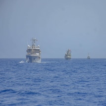 Three military vessels in a line at sea.