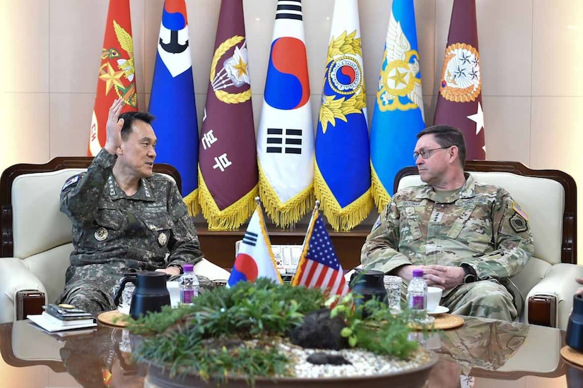 Two military officials sit in chairs and talk,
