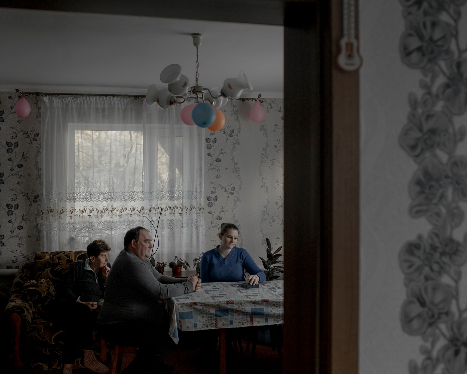 Viktoria Andrusha sits in her living room with her parents with balloons above.