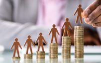 A stack of people figurines standing on piles of coins.