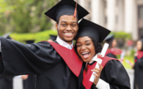 Two HBCU graduates smile for a photo on graduation day.