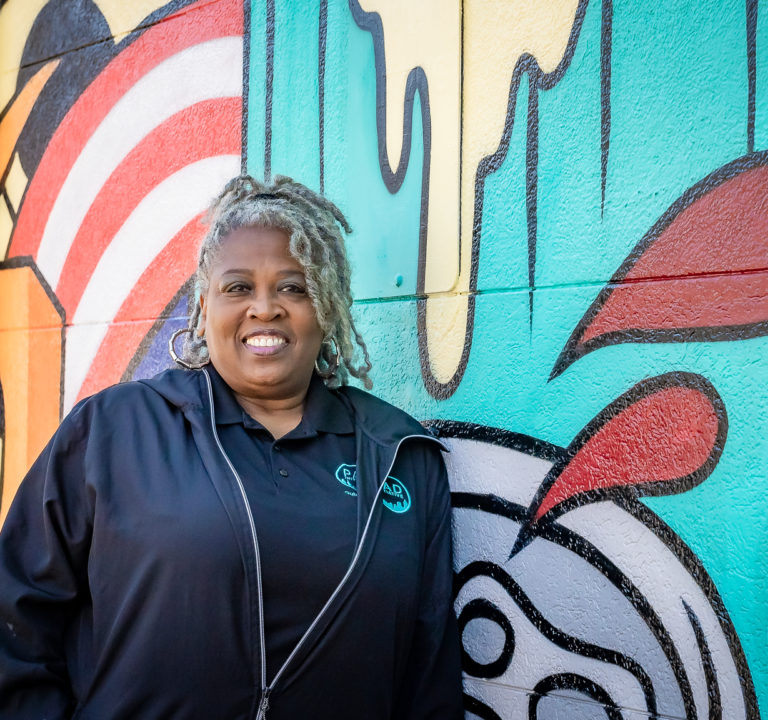 A woman smiles as she stands in front of a colorful wall of graphic art