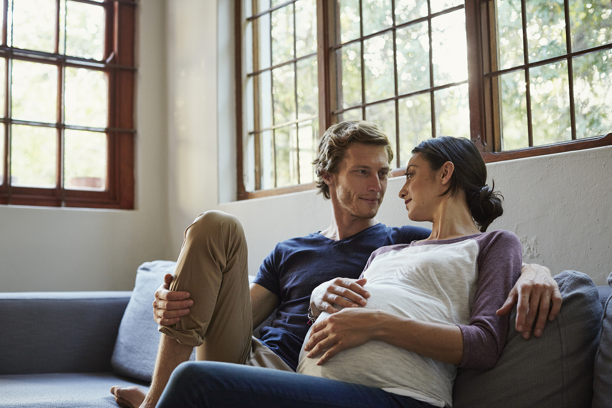 Loving expectant couple looking at each other while relaxing on sofa