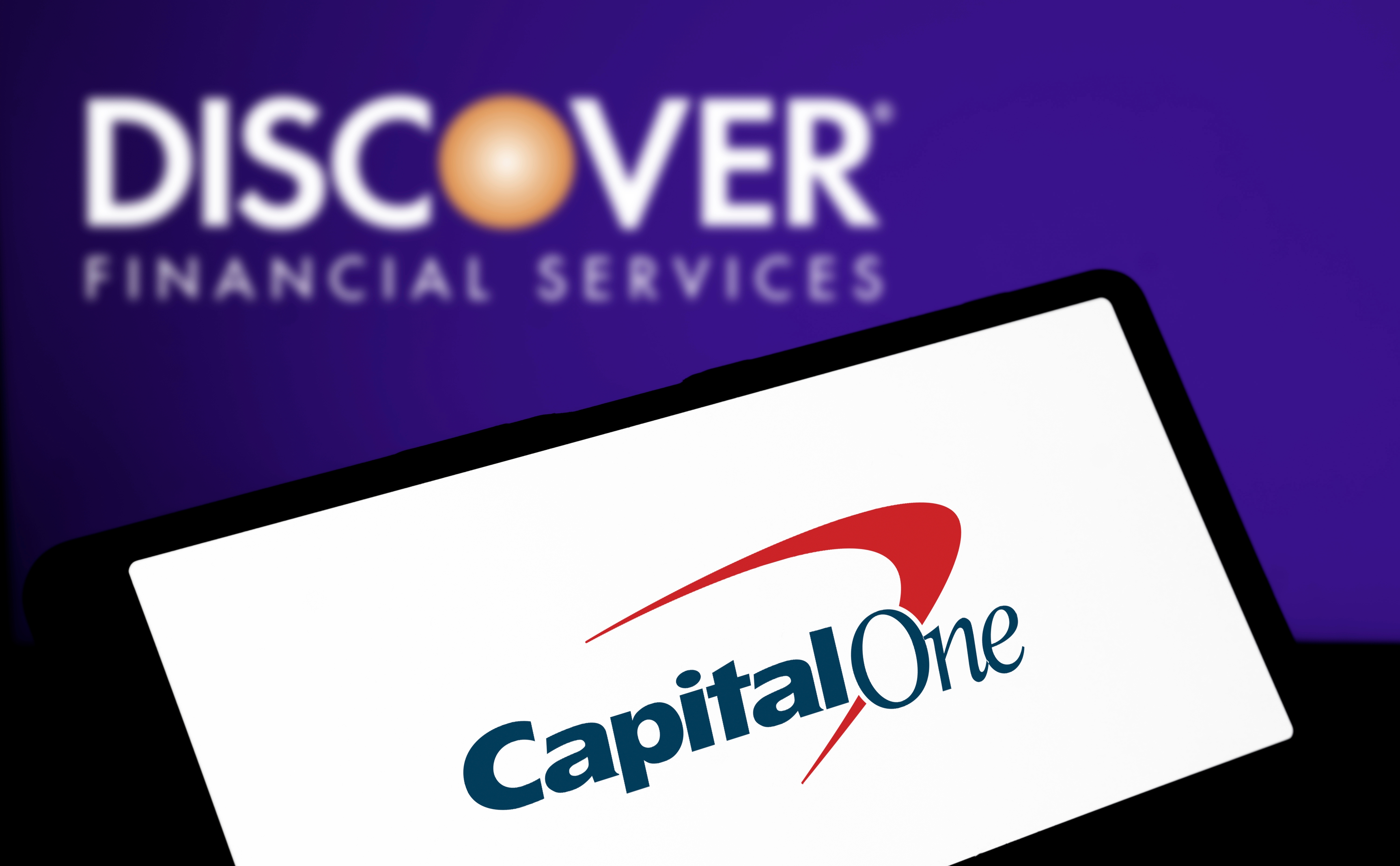 The Capital One website open on a laptop with the Discover logo in the background.