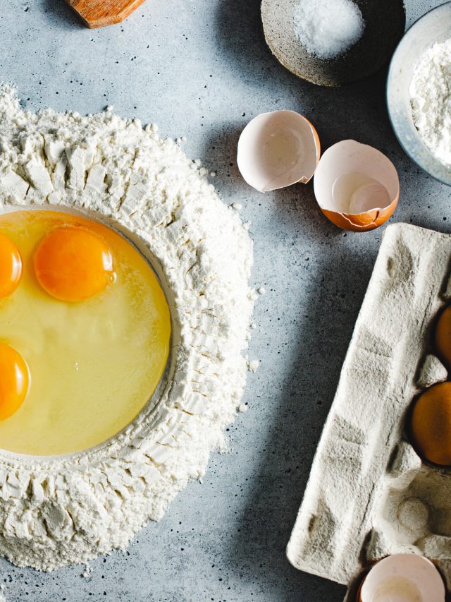 Eggs in a heap of flour surrounded by other ingredients.