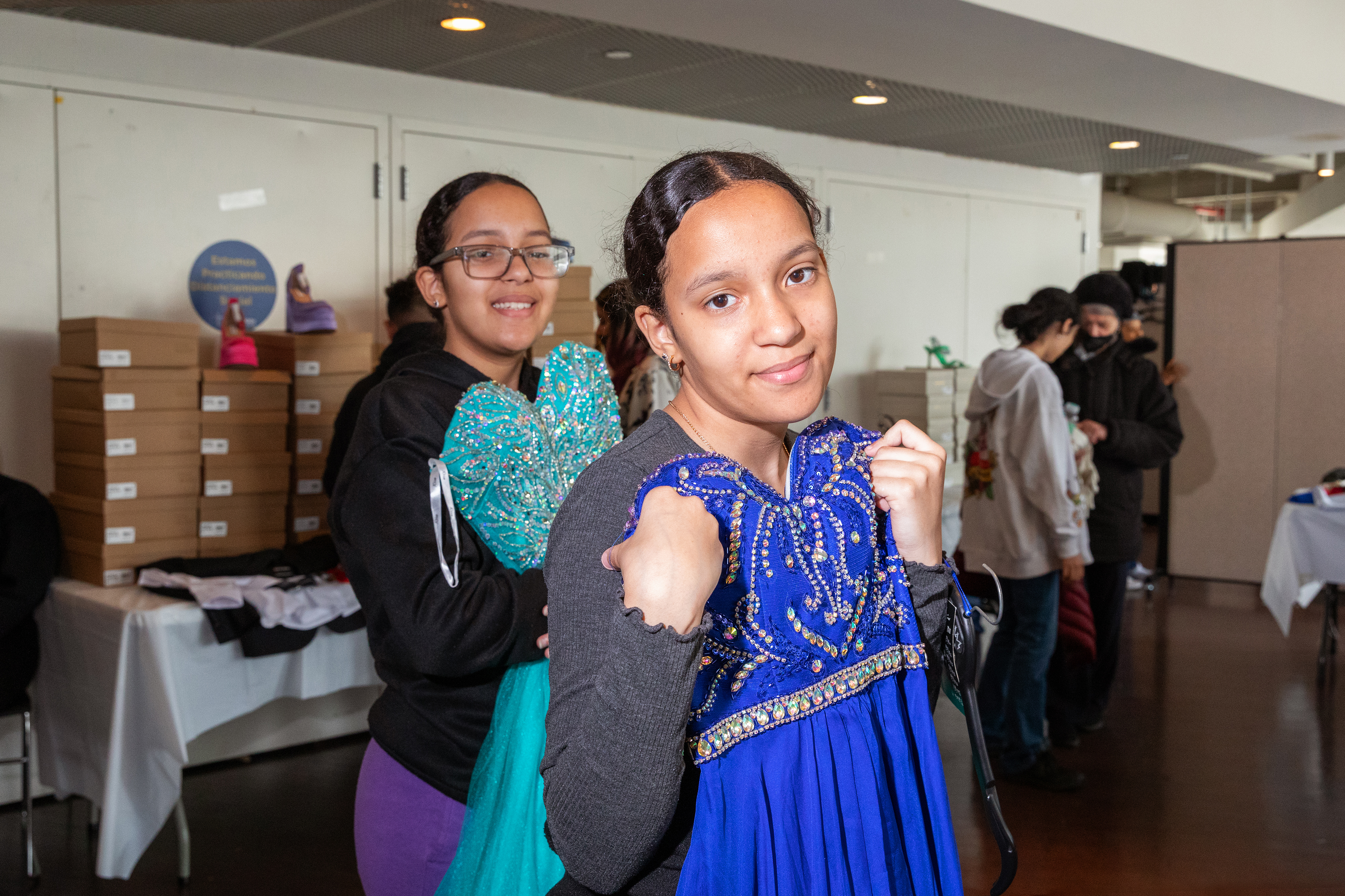Thirteen-year-old twins Crizzely and Crismayline holding and admiring prom dresses they selected at the Operation Prom clothing giveaway event