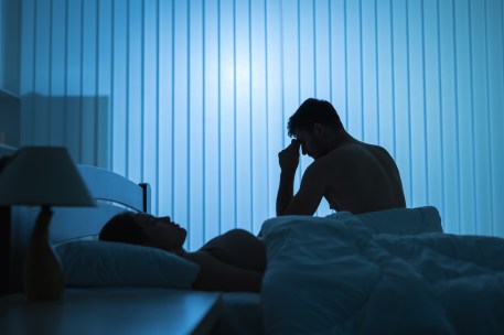 The worried man sit near near sleeping woman in the bed