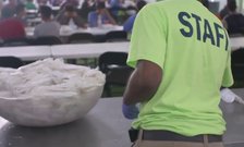 A person wearing a shirt that says "STAFF" in front of a bowl of silverware in a cafeteria