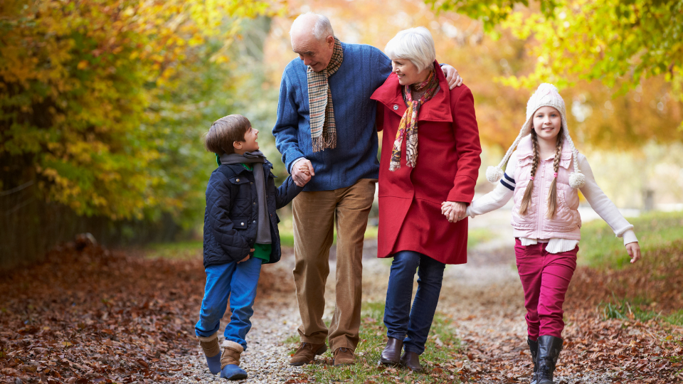 A photo of two grandparents walking hand in and with their grandchildren through an autumnal forest.