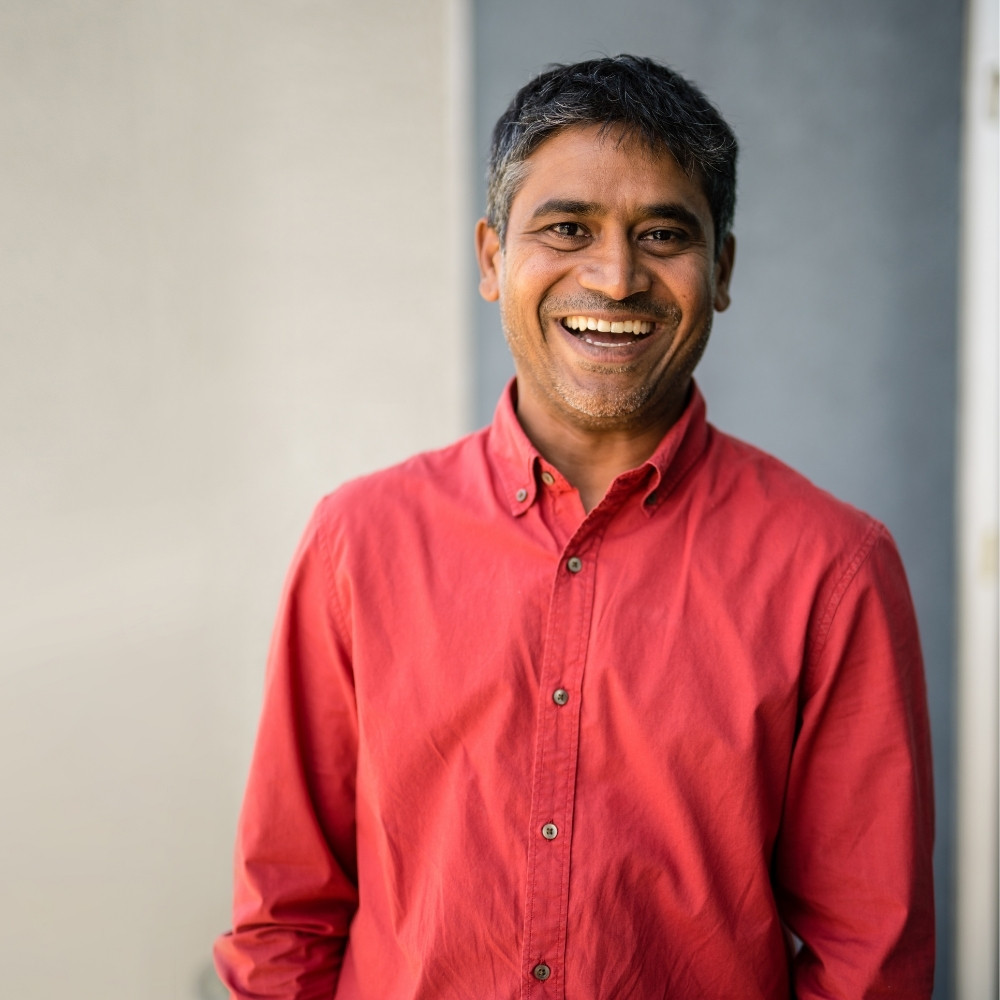 A smiling adult man standing in front of a building