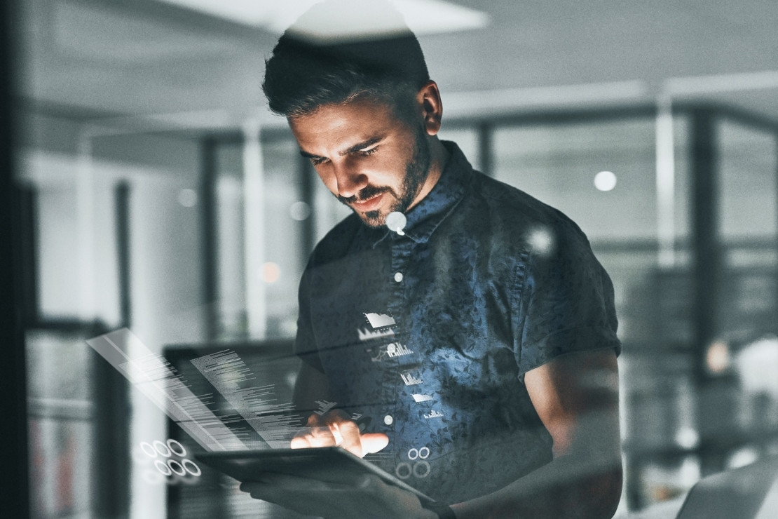 Adult man in a dim office holding a tablet surrounded by images of data floating around it.