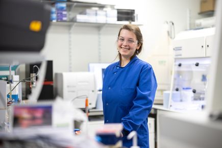 A woman in a lab wearing a blue lab coat and safety glasses