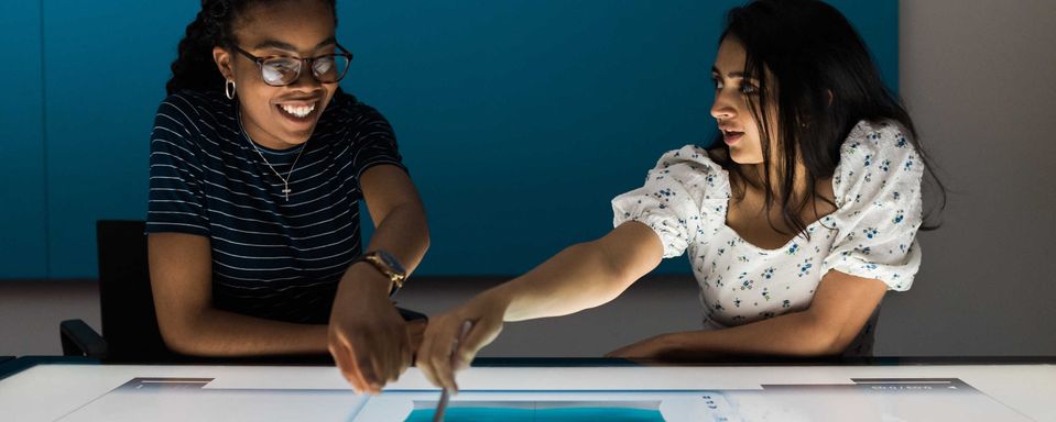 Two students illuminated by work on a table-sized screen