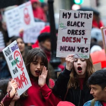 A blurred group of women marching at a protest. Some women are holding up signs, but only one can be read: 'My little black dress doesn't mean yes'.