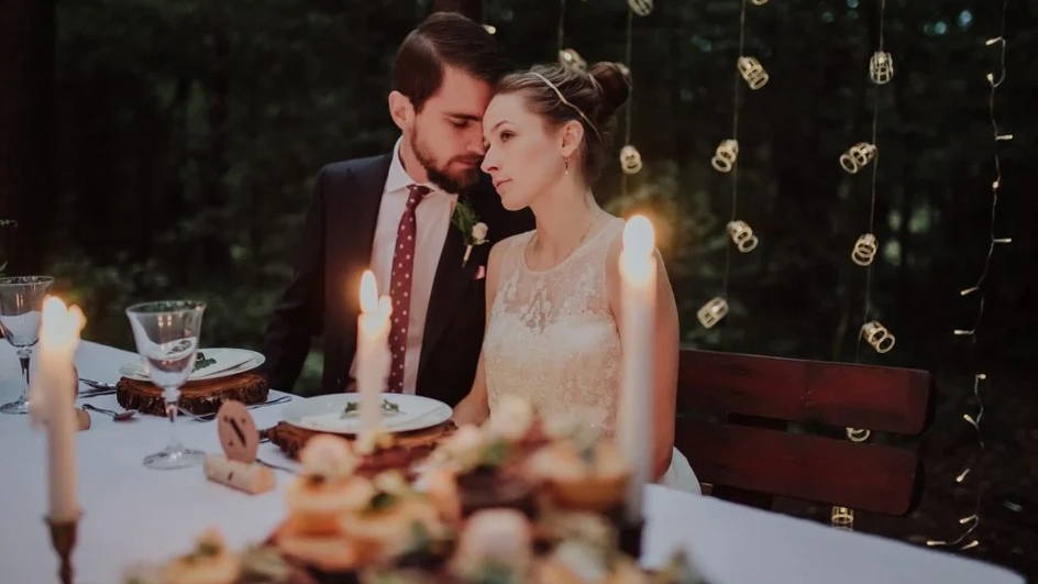 Жених и невеста сидят за столом, горят свечи.