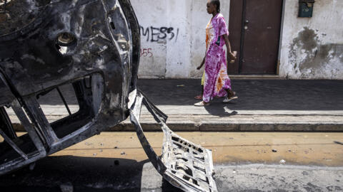 [Image d'illustration] Une femme passant devant une voiture incendiée à Dakar, le 5 juin 2023.