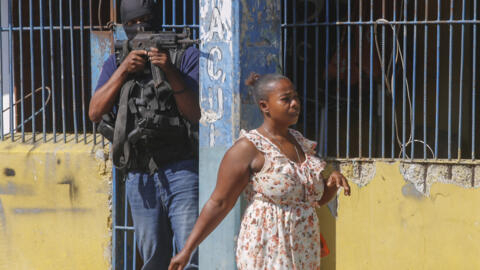A resident walks past a National Police officer guarding the empty National Penitentiary after a small fire inside the jail in downtown Port-au-Prince, Haiti, Haiti, Thursday, March 14, 2024.