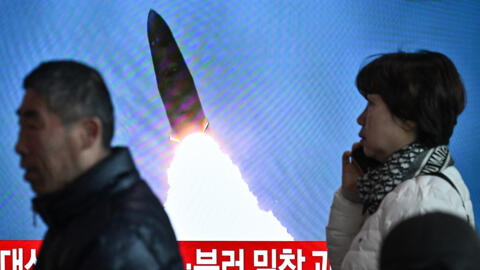 People walk past a television showing a news broadcast with file footage of a North Korean missile test, at a railway station in Seoul on March 18, 2024. 