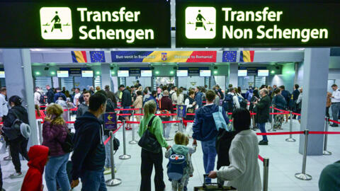 Travelers walk next to newly installed signs pointing to Schengen and non-Schengen areas minutes after midnight at Otopeni's "Henri Coanda" international airport on March 31, 2024.