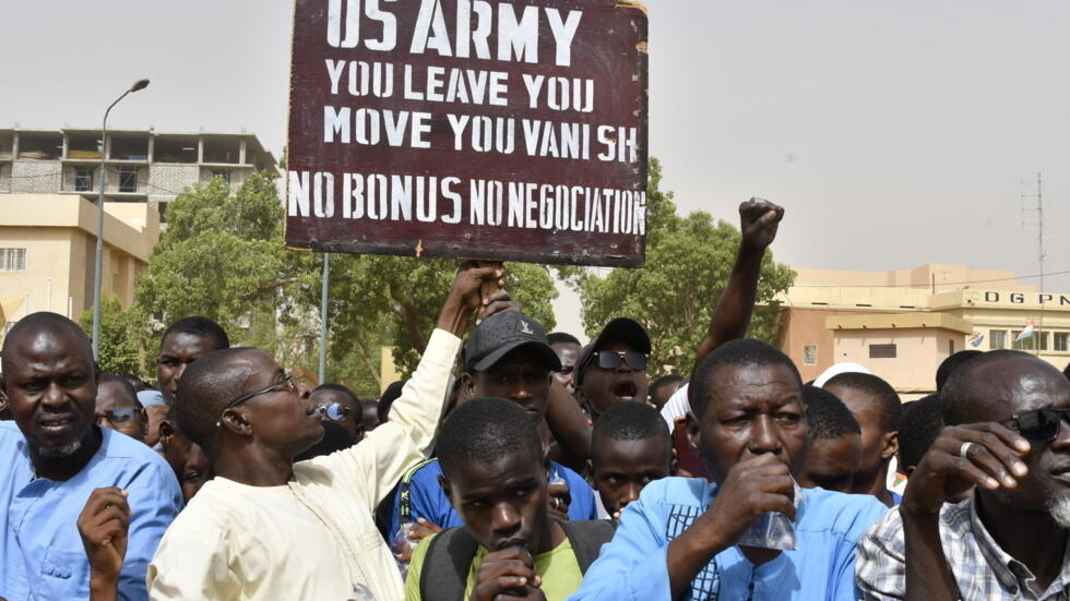 Protesters react as a man holds up a sign demanding that soldiers from the United States Army leave Niger without negotiation during a demonstration in Niamey, on April 13, 2024.