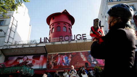 Parisians take pictures of the Moulin Rouge on April 25, 2024, after the blades on top of the landmark building fell off overnight.