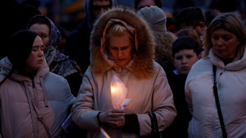 A woman holds a candle in front of a makeshift memorial to the victims of a shooting attack set up outside the Crocus City Hall concert venue in the Moscow region, March 23, 2024.