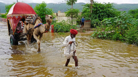 A man with his camel wade across a flooded street after heavy monsoon rains in Pushkar, in India's Rajasthan state on July 10, 2023.