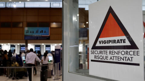 Passengers queue to check in next to a Vigipirate warning mesure sign (R) reading "reinforced security, terror attack risk" at the international airport in Cayenne, French Guiana on March 24, 2024.