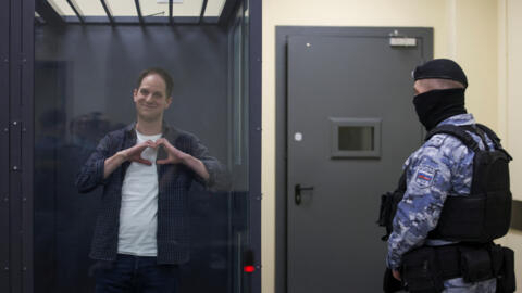 Wall Street Journal reporter Evan Gershkovich, who is in custody on espionage charges, makes a heart-shaped gesture inside an enclosure for defendants before a court hearing in Moscow, Russia.