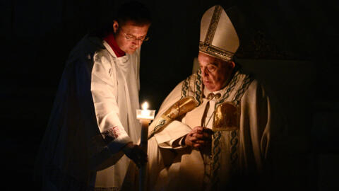 Pope Francis (R) looks at his candle during the Easter vigil as part of the Holy Week celebrations, at St Peter's Basilica in the Vatican on March 30, 2024.