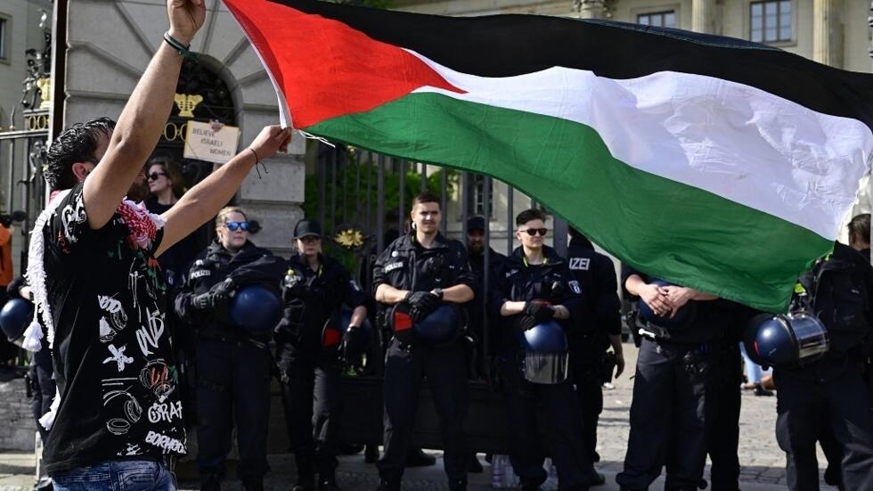 متظاهر يرفع العلم الفلسطيني بينما تغلق الشرطة مدخل جامعة هومبولت في برلين، أثناء اعتصام مؤيد لغزة وتضامنا مع الشعب الفلسطيني، في 3 مايو 2024.