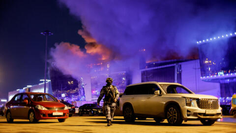 Сотрудник правоохранительных органов идет по парковке возле горящего концертного зала «Крокус Сити Холл», в котором вооруженные люди в камуфляже открыли стрельбу по пришедшим на концерт людям.