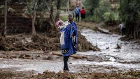 A woman carrying her baby on the back looks on near her house in a muddy area heavily affected by torrential rains and flash floods in Mai Mahiu, Kenya, on 29 April, 2024.
