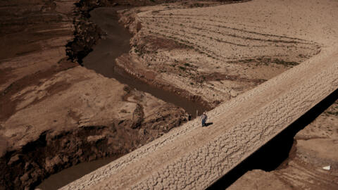 A man walks on the cracked ground of the Baells reservoir in Catalonia, Spain, in March 2023, as drinking water supplies have plunged to their lowest level since 1990 due to extreme drought.