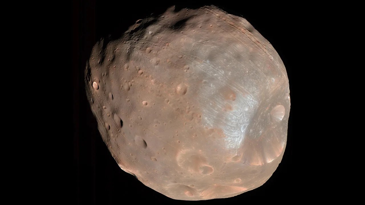 Roundish, reddish moon with massive crater on one end.