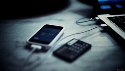 An iPhone charging next to a MacBook on a white table