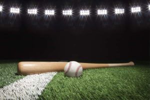 Baseball and bat at night under stadium lights on grass field with white stripe.