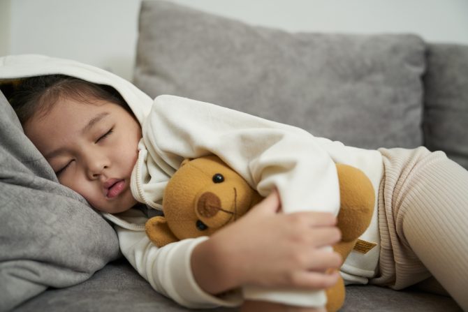 Sick Toddler girl with high flu and cold fever lying down on sofa